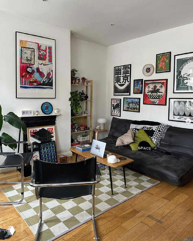 Уютная гостиная с чёрным диваном, креслом и стеной, покрытой оформленными арт-плакатами и растениями — пример UGC в интерьере.