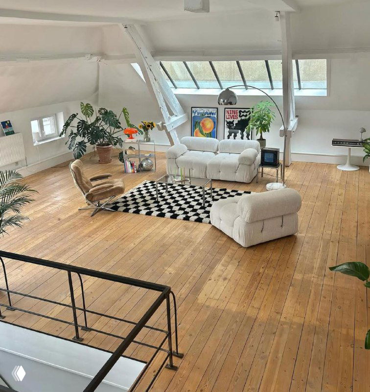 Большое мансардное пространство с белой софой, деревянным полом и несколькими постерами на стенах — светлый интерьер для вдохновения.