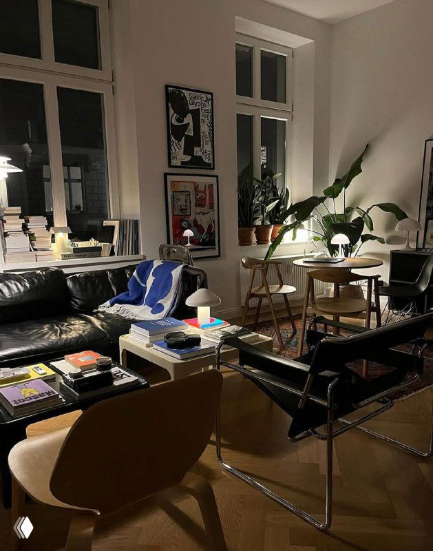 Ночной интерьер с диваном, журнальным столом и несколькими плакатами на стене; тёплое освещение подчёркивает атмосферу помещения.