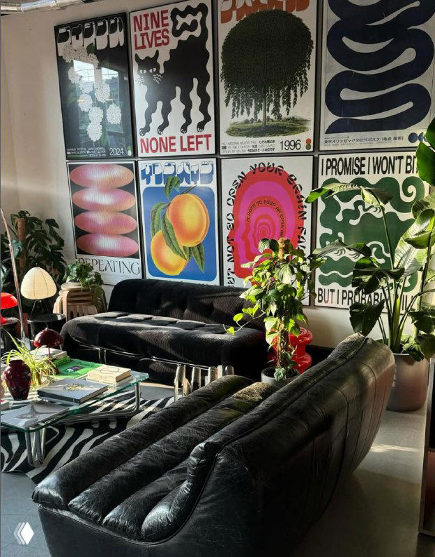 Комната с чёрным диваном и стеной, полностью покрытой разноформатными постерами — наглядный пример стен-галерей в домашних интерьерах.