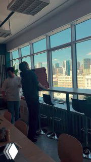 Кадр из рилса в офисном пространстве: люди переносят коробки у панорамных окон, визуал о совместных активностях и коллабах между брендами.