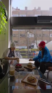 Два человека в кафе у окна с чашками и десертами; интерьер и уличный городской фон видны через витрину — кадр в стиле Reels для рекламы.