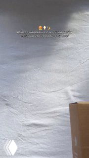 Крупный план мятой белой простыни на фоне; внизу справа частично видна картонная коробка — кадр из рекламного видео бренда YAM.