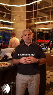 Кадр из ролика: мужчина в ресторане объясняет про новую пиццу, виден интерьер заведения и стол с тарелкой пиццы, автор проекта в кадре.