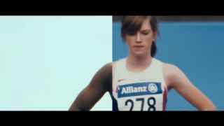 Кадр видеоролика: женщина-спортсменка в стартовом номере на дорожке, фрагмент динамичной спортивной сцены, использованный в рекламе.