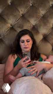 Женщина в постели кормит младенца на руках на фоне мягкого высоко оформленного изголовья — кадр из обсуждаемого вертикального видео.