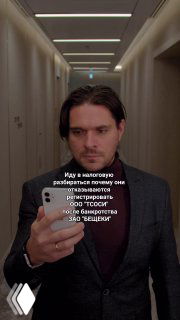 Вертикальный видеокадр: мужчина в коридоре держит телефон и делает селфи-видео, на экране виден наложенный юмористический текст.