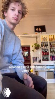 Парень в своей небольшой кофейне внутри художественного магазина, на заднем плане полки с напитками и барная стойка — вертикальное видео с подписью 'Starting a cafe'.