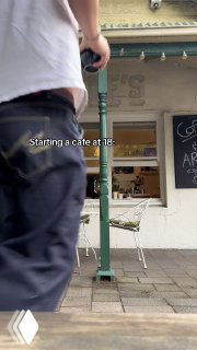 Уличный кадр у входа в кофейню: часть фасада, столики и вывеска, кадр вертикального видео с подписью о старте кафе в 18 лет.