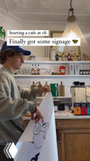 Интерьер кафе: барная стойка, полки с бутылками и напитками, молодой человек за прилавком — кадр процесса и повседневной работы заведения.