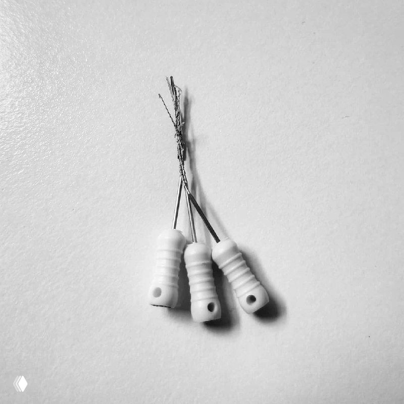 Чёрно‑белая фотография трёх H‑файлов с закрученными металлическими нитями, демонстрирующая приём «косичка» при извлечении эндодонтических обломков