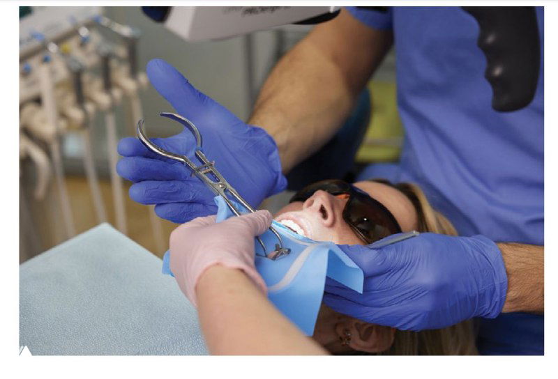 Врач и ассистент передают инструменты через коффердам: руки в перчатках, направленная передача инструментов, фокус на эргономике рабочей зоны.