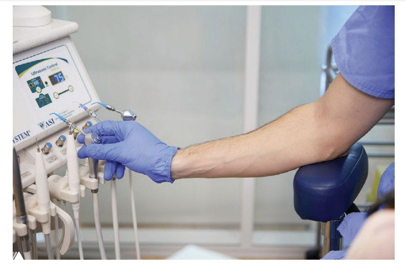 Рука врача регулирует элементы на стоматологическом блоке: управление наконечниками и ирригацией в пределах досягаемости рабочего круга.