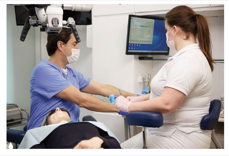 Врач и ассистент работают синхронно: ассистент передаёт инструмент, врач держит микроскоп — сцена командной работы в эргономичном кабинете.