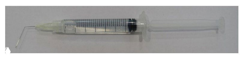 Пластиковый ирригационный шприц с прикреплённой иглой в блистере на светлом фоне; крупный план для демонстрации изгиба и размеров канюли.