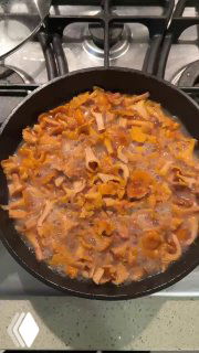 Крупный план сковороды на плите: ярко-оранжевые лисички жарятся в масле — процесс приготовления ужина.