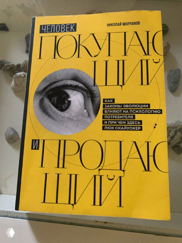 Жёлтая обложка книги «Человек покупающий и продающий» на столе; заметен крупный художественный элемент — рисунок глаза, и чёткая типографика названия.