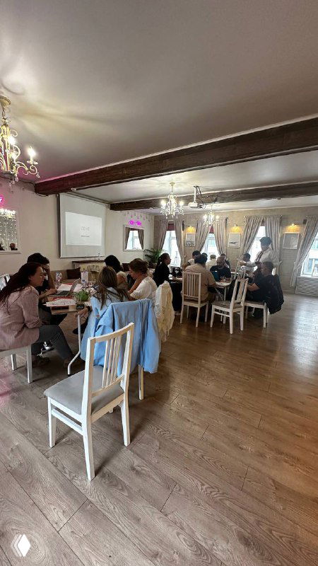 Участники бизнес‑игры в светлом зале: команды за столами обсуждают кейсы, на стене виден экран с презентацией и розовая декоративная подсветка.