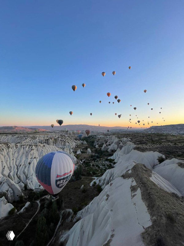 Утреннее небо с множеством воздушных шаров над уникальным каменным ландшафтом Каппадокии; вид на полёт шаров и долины при рассвете.