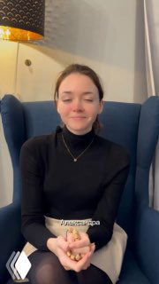 Женщина в тёмной водолазке сидит в мягком кресле с закрытыми глазами и сложенными руками;спокойный интерьер и лампа в кадре.