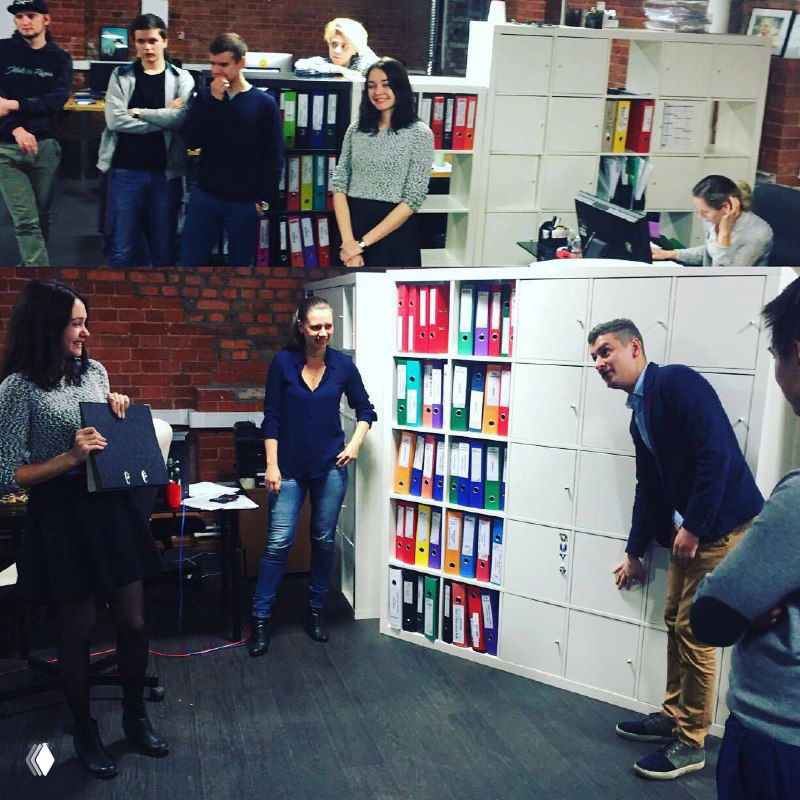 Группа сотрудников в офисе у стеллажей с папками; кадр показывает живое обсуждение проекта и командную работу в офисной среде EdTech-команды.