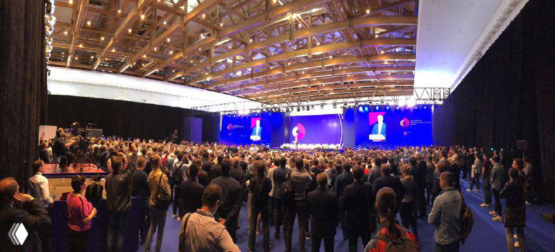 Большой конференц-зал с множеством людей на фоне сцены и экранов — иллюстрация формата выступлений и PR-ивентов, о которых пишет автор.