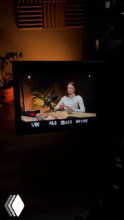 Съёмка через экран камеры: женщина-эксперт сидит в студии во время записи, видны свет, микрофон и часть декорации