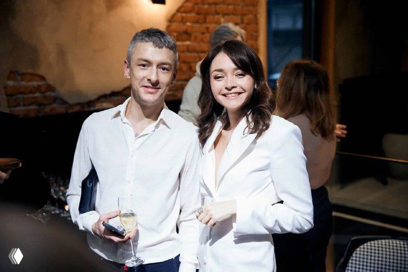 Женщина и мужчина в светлой одежде на деловой встрече в интерьере с кирпичной стеной; видно атмосферу бизнес‑мероприятия и нетворкинга.