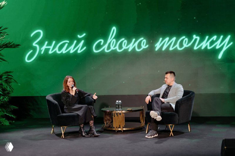 Фотография мастер-класса: два спикера сидят в креслах и беседуют на сцене перед зелёным фоном с неоновой надписью.