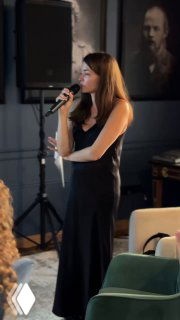 Женщина выступает с микрофоном на профессиональном мероприятии; видна сцена, часть аудитории и деловая атмосфера EdTech-события