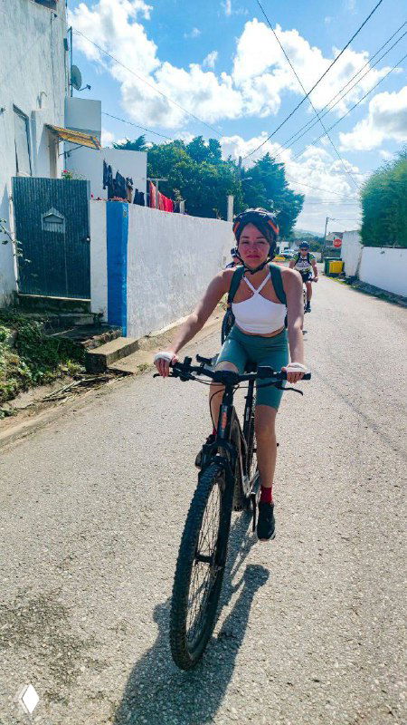 Человек на велосипеде по солнечной улице жилого района; изображение передаёт движение, свободу и символ личного роста.