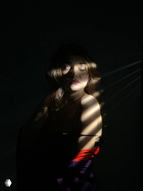 Женщина в ярком красном платье в полумраке, свет и тень падают на лицо и плечи — образ силы, сексуальности и уверенности автора.