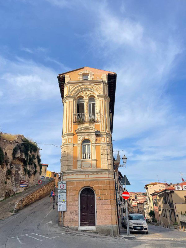 Высокий узкий дом у перекрёстка на фоне голубого неба — характерная архитектура маленького итальянского прибрежного городка на острове Эльба.