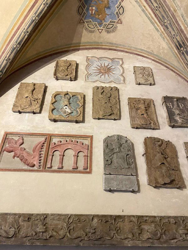 Стена с многочисленными каменными барельефами и архитектурными фрагментами в музее Барджелло: средневековые рельефы и декоративные элементы.