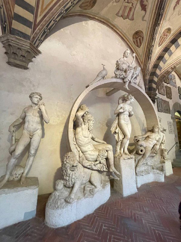 Скульптурная группа в арочном проёме Барджелло: композиция с несколькими фигурами и декоративными элементами, вид со стороны зала.