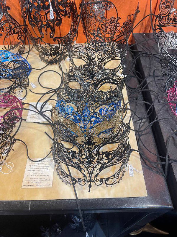 Витрина с ажурными венецианскими масками разных форм и узоров, крупный план сувениров в магазине на туристической улице.