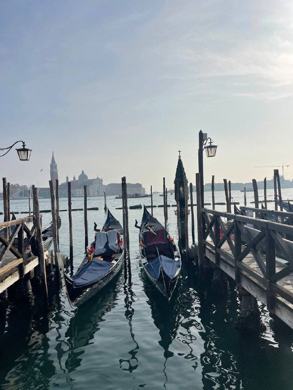 Причал с гондолами на воде, вид на лагуну и силуэты островов вдали; спокойное утреннее море и традиционные лодки у причала.