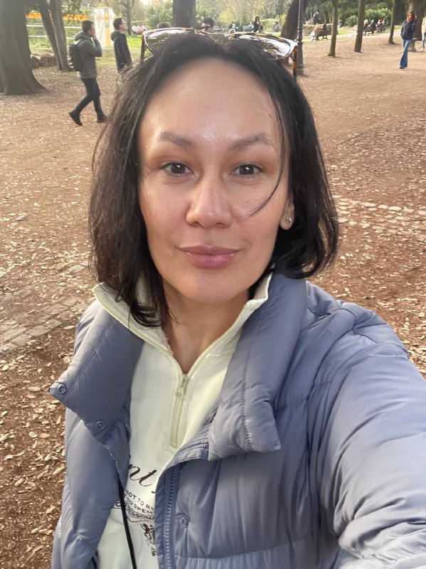 Портретное селфи на открытом воздухе в парковой зоне Рима: человек в тёплой куртке на фоне деревьев и дорожек.