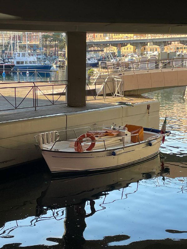 Небольшая прогулочная лодка в генуэзской марине, стоящая рядом с причалом: четкие отражения и спокойная вода в гавани.