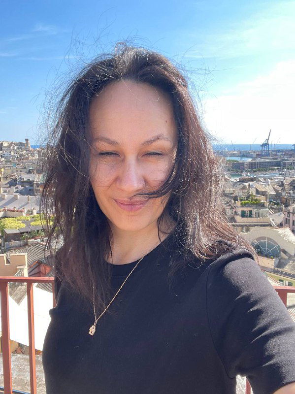 Портрет автора на фоне крыши и гавани Генуи: улыбающееся лицо на солнце, вдалеке виднеются море и городской пейзаж.