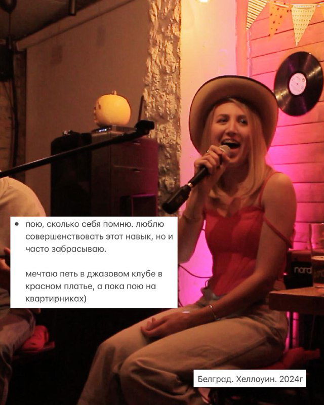 Маша поёт в клубе с микрофоном в руках, яркое сценическое освещение и виниловая пластинка на стене создают атмосферу живого выступления и путешествий по городам.