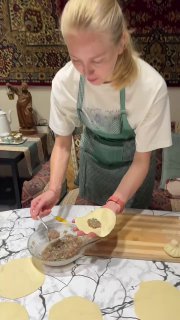 Инструктор на мастер-классе лепит хинкали: видны круглые заготовки теста и ложка с начинкой на рабочей поверхности кухни.