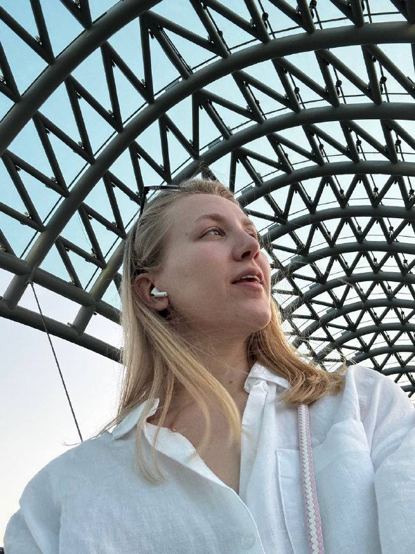 Селфи человека на пешеходном мосту в Тбилиси: металлическая арочная конструкция образует сетчатый купол над прогулочной зоной на фоне неба.