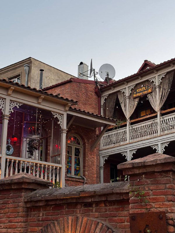 Кафе и традиционные балконы на кирпичном фасаде старого квартала Тбилиси: вывески, тёплые огни и атмосфера вечерней прогулки по городу.