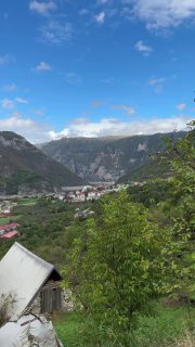 Вид на новый город Плужине у подножия гор рядом с Пивским озером: домики в долине, зелёные склоны и горные вершины на горизонте.