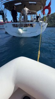 Вид из тузика на корму яхты-магазина: люди на палубе, швартовочный трос и часть надувного борта внизу кадра, сцена с морским бытом.