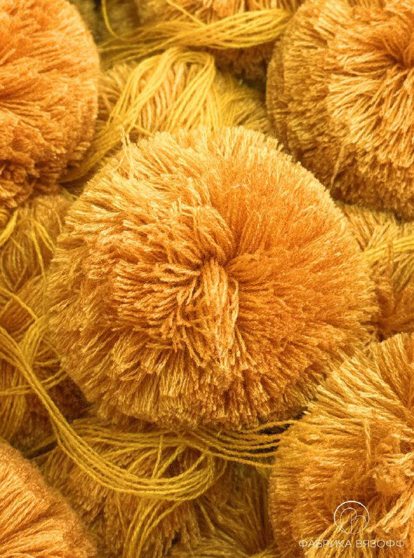 Детальная съёмка одного крупного жёлтого помпона из нитей; видно плотное переплетение пряжи, ворс и структуру для устойчивого крепления.