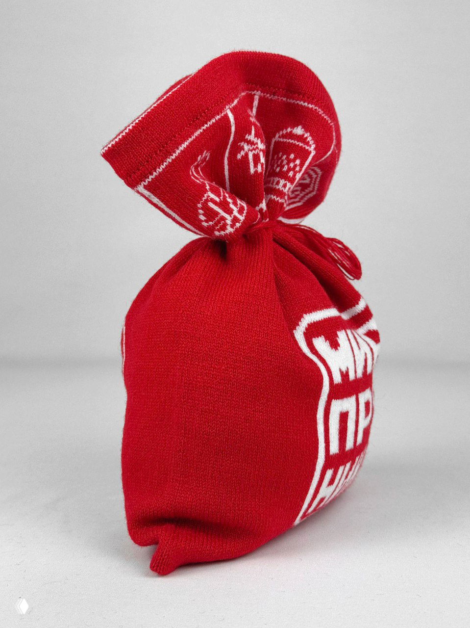 Боковой ракурс красного вязаного мешочка: плотная текстура полотна, частичный логотип «Мир пряника» и аккуратный профиль изделия на нейтральном фоне.