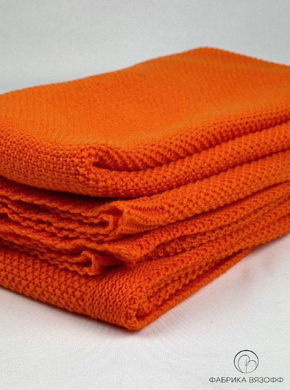 Сложенный в несколько слоев оранжевый вязаный плед; кадр демонстрирует толщину, плотность вязки и аккуратные линии сгибов.
