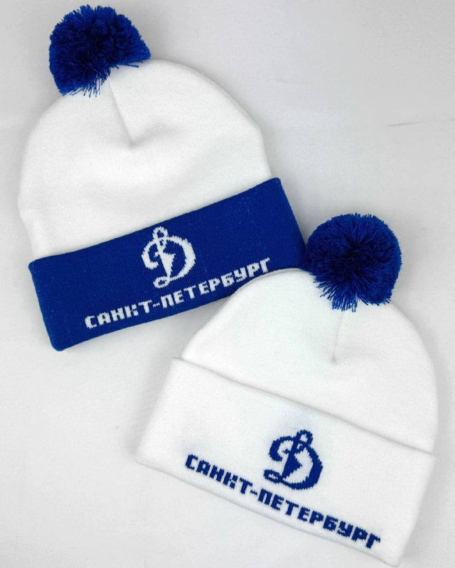Две вязаные шапки белого и синего цветов с отворотами и помпонами, на отвороте — вышитый или провязанный логотип и надпись «Санкт‑Петербург».
